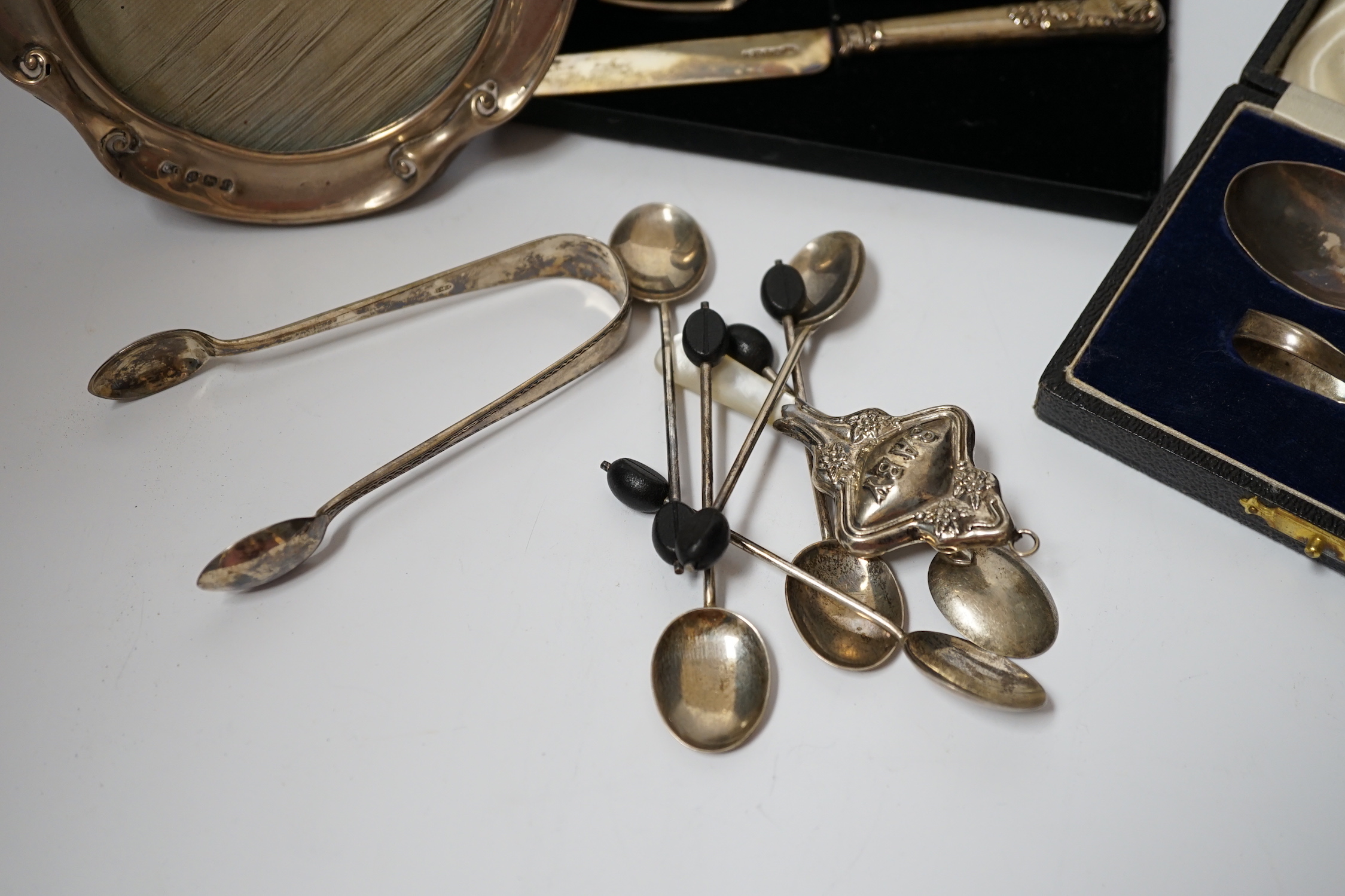 A cased silver christening spoon & pusher, a Georgian silver christening knife and fork, six silver bean end coffee spoons, a child's silver rattle, silver sugar tongs and a silver mounted photograph frame, Birmingham, 1